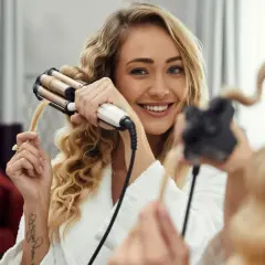Uśmiechnięta blondynka tworzy sobie fale hollywoodzkie za pomocą lokówki.