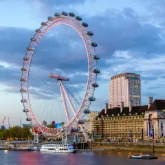London Eye oświetlone wieczorem, z widokiem na Tamizę i budynki w tle.