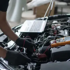 Mechanik diagnozuje objawy pompy wysokiego ciśnienia 1.6 THP za pomocą multimetru i laptopa przy otwartej masce samochodu.