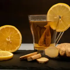 Kiedy dodać cytrynę do herbaty? Zaparzona herbata z plasterkiem cytryny, imbirem i połówką cytryny na czarnym tle.