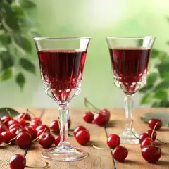 Dwa kieliszki z rubinowym alkoholem z wiśni, otoczone świeżymi owocami i zielonymi liśćmi.