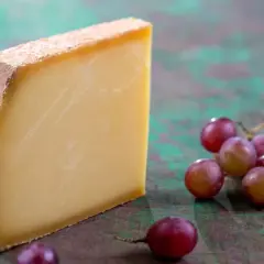 Un morceau de Comté aux cristaux savoureux, accompagné de grappes de raisins rouges sur un fond texturé.