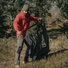 Mężczyzna w czerwonej kurtce i zielonej czapce składa zielony namiot w lesie. Pranie namiotu po wyprawie.