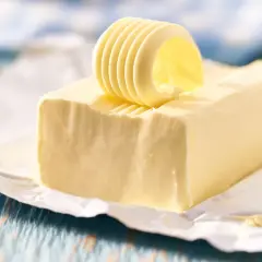 Un rouleau de beurre jaune, frais et crémeux, est posé sur un bloc de beurre, prêt à être tartiné.