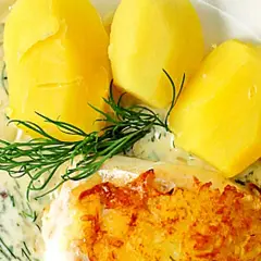 En gyllene fiskbit med krämig dillsås till fisk, serverad med kokt potatis och en citronskiva.