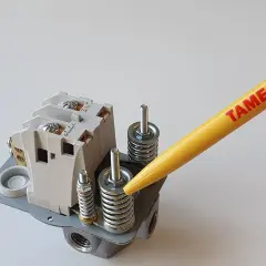 Ein gelber Stift mit der Aufschrift "TAMESON" zeigt auf die Federn eines Druckschalters, um den kompressor druck einstellen zu können.