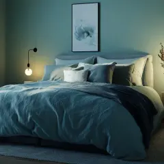 Gemütliches Schlafzimmer mit einer warmen Farbpalette aus Blau- und Grüntönen. Ein großes Bett mit vielen Kissen lädt zum Entspannen ein.