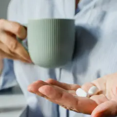 Osoba trzyma kubek i tabletki, przygotowując się do leczenia pod okiem hepatologa.