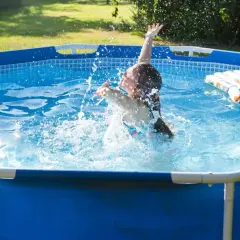 Dziewczynka pluska się w basenie ogrodowym, tworząc fontannę wody. To idealny basen do ogrodu na upalne dni.