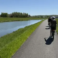 Rodzina na rowerach wzdłuż kanału. Słoneczny dzień sprzyja rodzinnemu **velo skawa** pośród zielonych łąk i drzew.