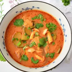 Aromaticzna zupa tom yum z kurczakiem, grzybami i kolendrą w misce z niebieskim wzorem. Obok leży łyżka.