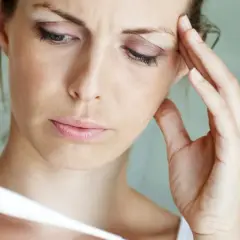 Frau mit Fieber, die sich die Stirn hält und ein Thermometer betrachtet. Psychosomatischer Fieber kann viele Ursachen haben.