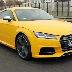 Żółte Audi TT RS, jedna z nowszych audi tt generacji, pędzi po drodze.