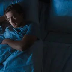 Ein Mann schläft tief und fest im blauen Licht. Manchmal fragt man sich, ob man zu viel schlafen kann.