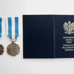 Dwa medale z czerwonym krzyżem i napisem "Honorowy Dawca Krwi Zasłużony dla Zdrowia Narodu" oraz granatowa teczka z godłem Polski.