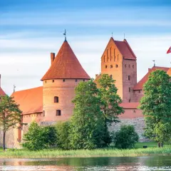 Zamek w Trokach, majestatyczna ceglana twierdza z czerwonymi dachami, wznosi się nad wodą, otoczony zielenią.