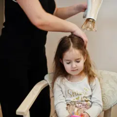 Mama suszy włosy córki suszarką, dbając o delikatną pielęgnację włosów dziecka.