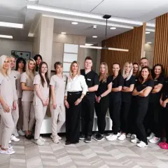 Zespół stomatologów i personelu medycznego w jasnych i ciemnych uniformach stoi w gabinecie.