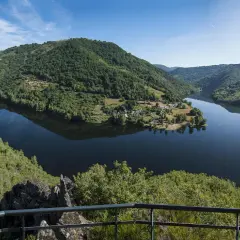 Vue panoramique des gorges de la Truyère, avec un lac paisible reflétant les collines verdoyantes et un village pittoresque.