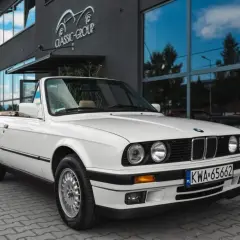 Białe bmw e30 cabrio z beżowym wnętrzem zaparkowane przed budynkiem z napisem "Classic Group".