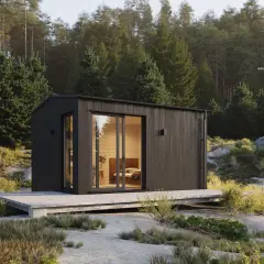 Modern friggebod med stora fönster, omgiven av skog och sten. Drömmen om att bygga friggebod blir verklighet.