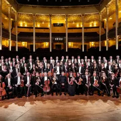 Kungliga Filharmonikerna medlemmar poserar i en stor orkestersal.