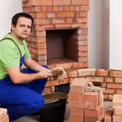 Murarz nakłada zaprawę na cegłę szamotową, budując kominek.