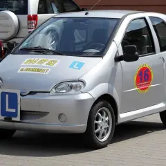 Srebrny czterokołowiec z literą "L" na masce i z boku, gotowy do nauki jazdy.
