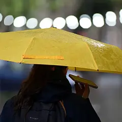 Una persona con un paraguas amarillo, bajo la lluvia, parece soñar con un día soleado mientras habla por teléfono.