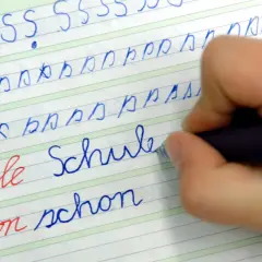 Kind übt das **Buchstaben schreiben lernen** auf liniiertem Papier. Es schreibt die Buchstaben S, b, p und die Wörter "Schule" und "schon".