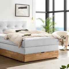 Ein hellgraues Boxspringbett mit Holzsockel und einem gesteppten Kopfteil. Die Nachteile eines Boxspringbetts, wie z.B. die Höhe, sind hier nicht ersichtlich.