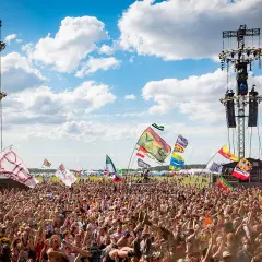 Tłum ludzi na festiwalu pod sceną z wieżami nagłośnieniowymi i flagami.