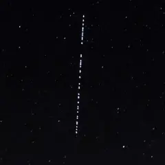 Nocne niebo z gwiazdami i pionowym sznurkiem jasnych punktów, przypominających przeloty Starlink.