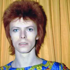 Ikoniczny David Bowie z burzą rudych włosów i niebieskimi oczami, w stroju przypominającym jego słynne kreacje. Jego muzyka, jak te utwory, wciąż inspiruje.