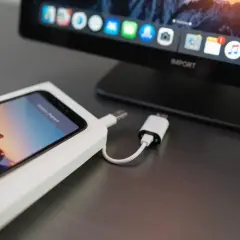 iPhone podłączony kablem do komputera z widocznym ekranem i ikonami aplikacji.