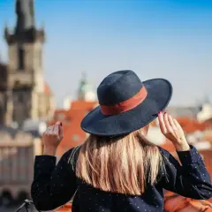 Kobieta w kapeluszu na tle europejskiego miasta.