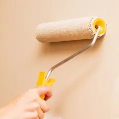 Mano che usa un rullo per pitturare una parete di color sabbia. Impara come pitturare con il rullo per un risultato perfetto.