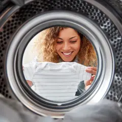 Uśmiechnięta kobieta wkłada ubranko do suszarki bębnowej Whirlpool.