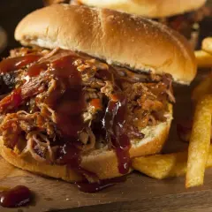 Un succulento panino con pulled pork, ricoperto di salsa barbecue, servito con patatine fritte croccanti.