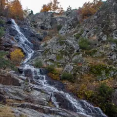 Cascada de Mojonavalle en otoño, con rocas cubiertas de musgo y árboles de hojas doradas.