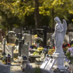Kamienna anielica na cmentarzu, otoczona nagrobkami i zniczami. Pytanie, czy na cmentarzu można palić, pozostaje otwarte.