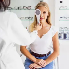 Kobieta przechodzi badanie wzroku, zasłonięte jedno oko. Optometrysta wykonuje cover test.