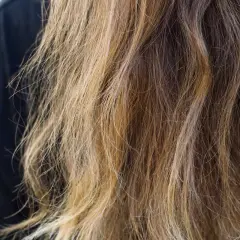 Chevelure châtain aux reflets blonds, légèrement ondulée, montrant l'effet de l'eau sur les cheveux.