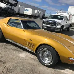 Złoty Chevrolet Corvette Stingray, jeden z klasycznych, sportowych aut, zaparkowany obok białej ciężarówki.