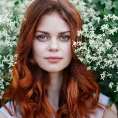Eine Frau mit leuchtend roten, bunten Haaren blickt aus einem Meer von weißen Blüten.