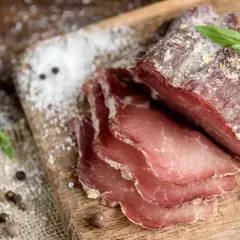 Pokrojone wędzone mięso na desce, obok czosnek i przyprawy. Idealne do peklowania mięsa przepis.