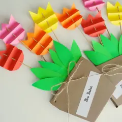 Kolorowe kwiaty z papieru, praca plastyczna "kwiaty dla babci i dziadka". Dwa bukieciki w brązowych opakowaniach z zielonymi liśćmi.