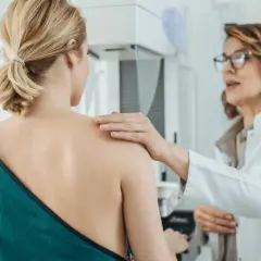 Ärztin legt Hand auf Schulter einer Patientin während einer Mammographie mit Implantaten.