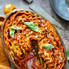 Lasagne aubergine italienne gratinée, garnie de feuilles de basilic frais, dans un plat ovale en terre cuite.