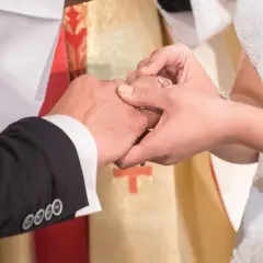 Podczas ślubu kościelnego w innej parafii, narzeczona zakłada obrączkę. W tle widać księdza w szacie liturgicznej.